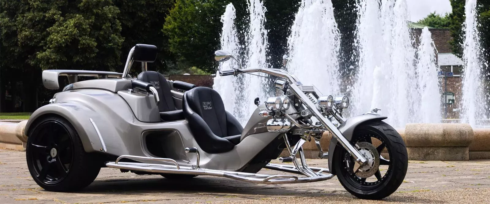 Silver Rewaco RF1 GTR trike parked in front of park fountains