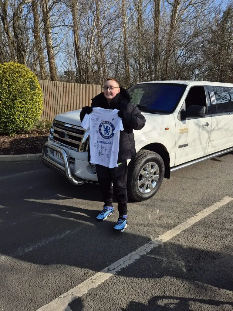 Young guest holding up a signed Chelsea shirt beside a white Starlite limousine