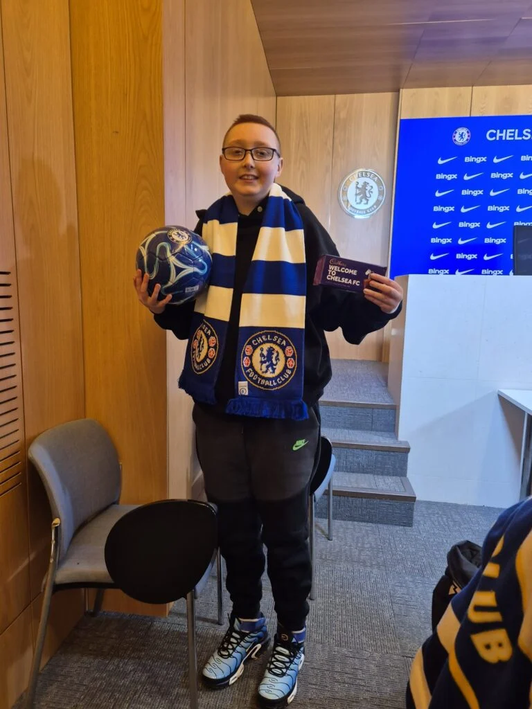 Young Chelsea fan holding a signed football and scarf in the press room