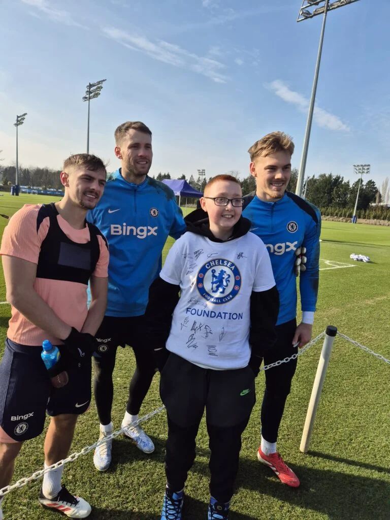 Young fan in a signed Chelsea Foundation shirt with three players on the training pitch